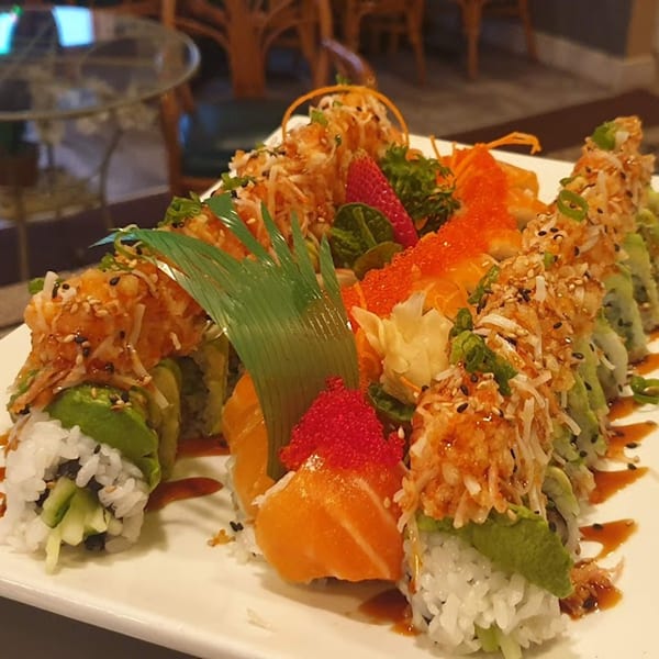 A large platter of colorful sushi rolls with avocado, salmon, roe, and crispy toppings.
